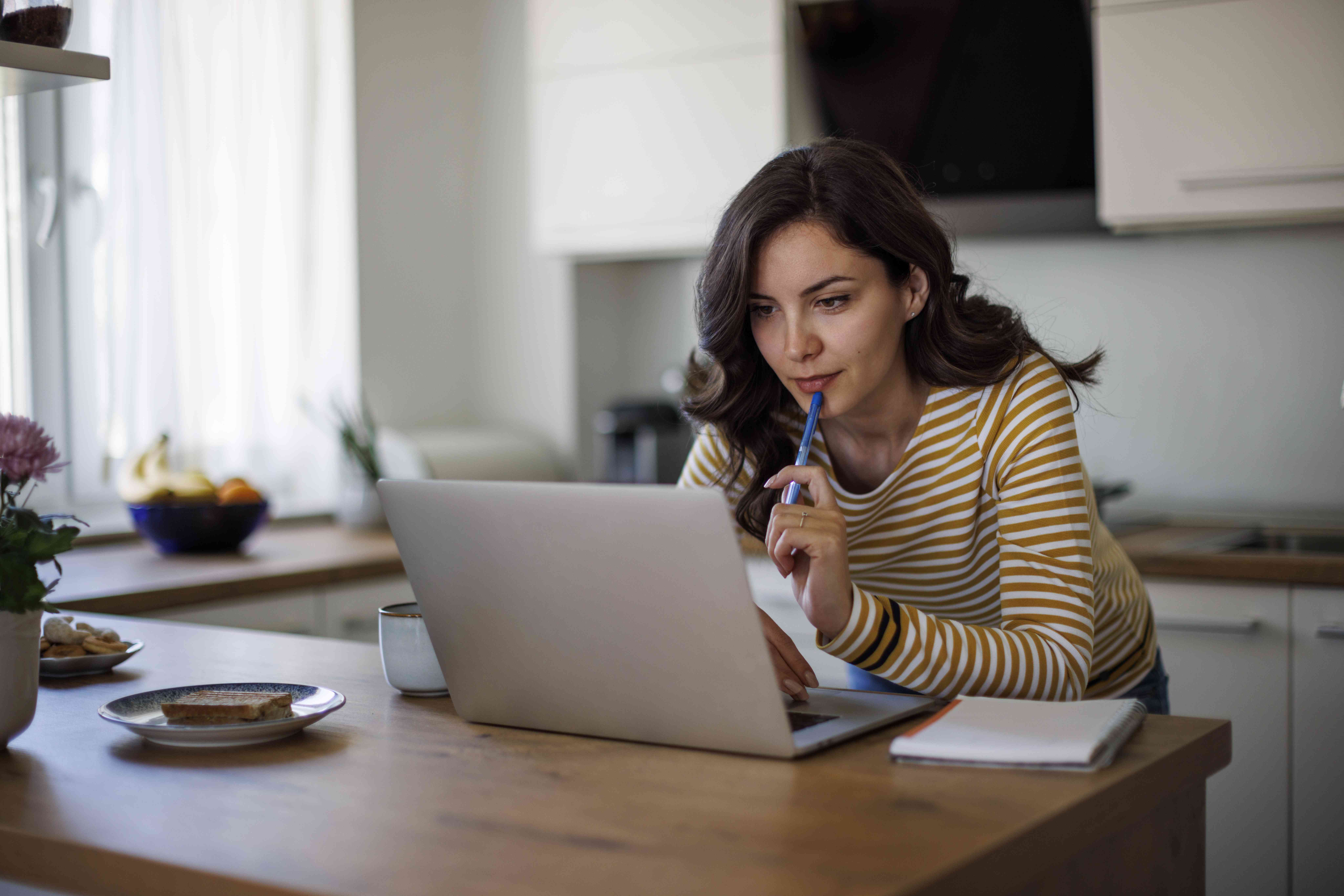 An investor leans over the kitchen counter while examining investment opportunities on a laptop.