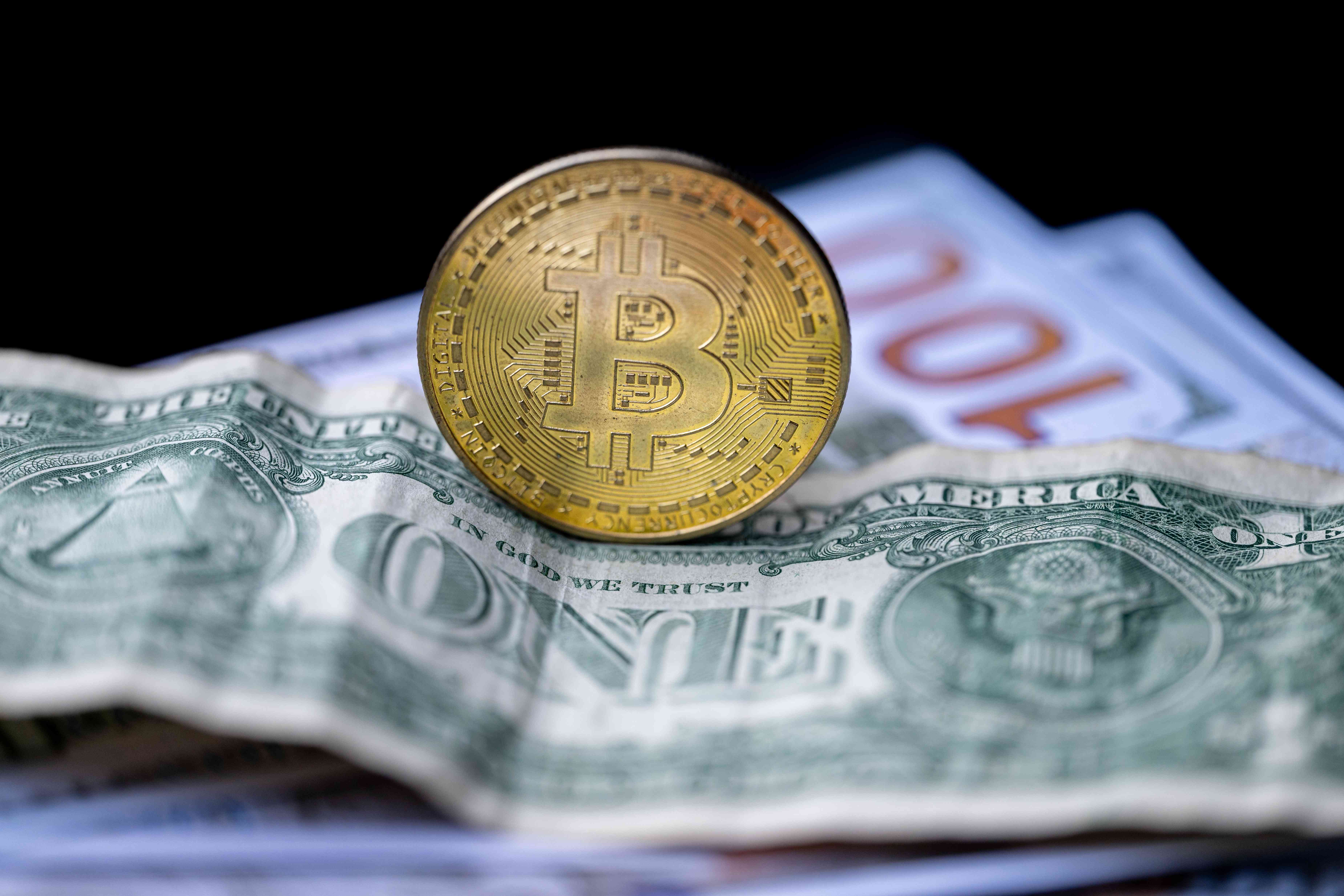 A representation of a Bitcoin appears on a U.S. dollar bill.