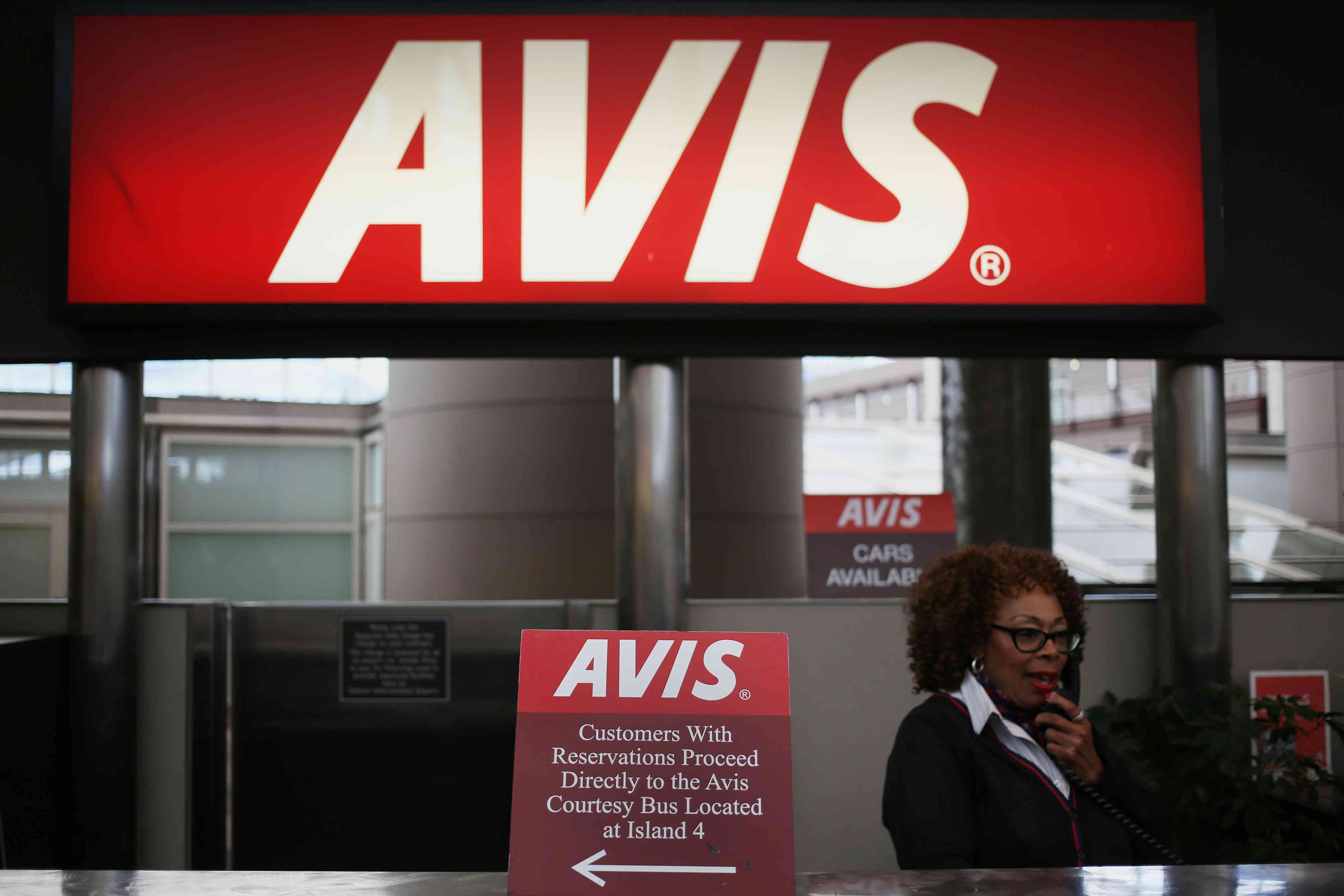An employee speaks on a telephone at a rental counter for Avis Budget Group at an airport.